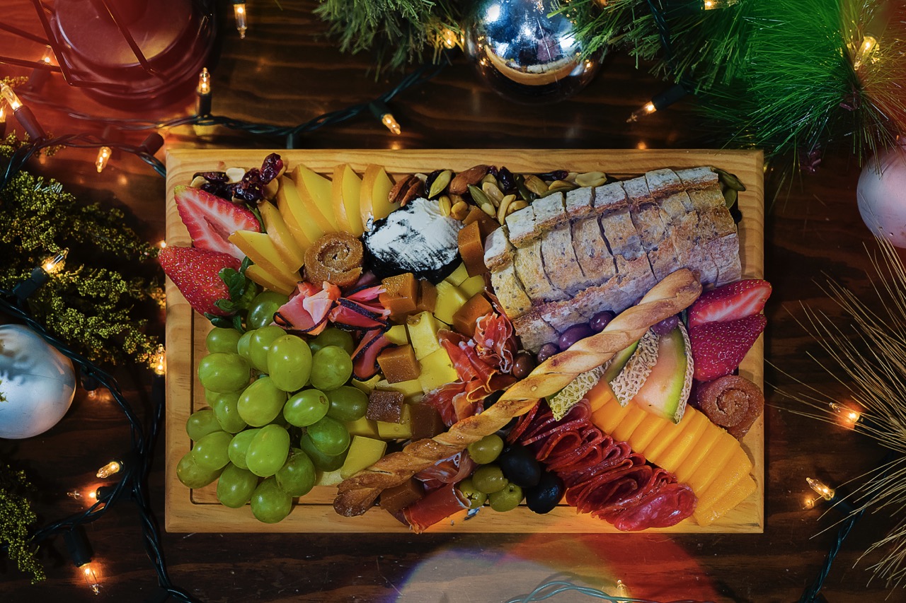 Christmas charcuterie board with fruits, cheeses, cold cuts, and bread on wooden board in festive environment