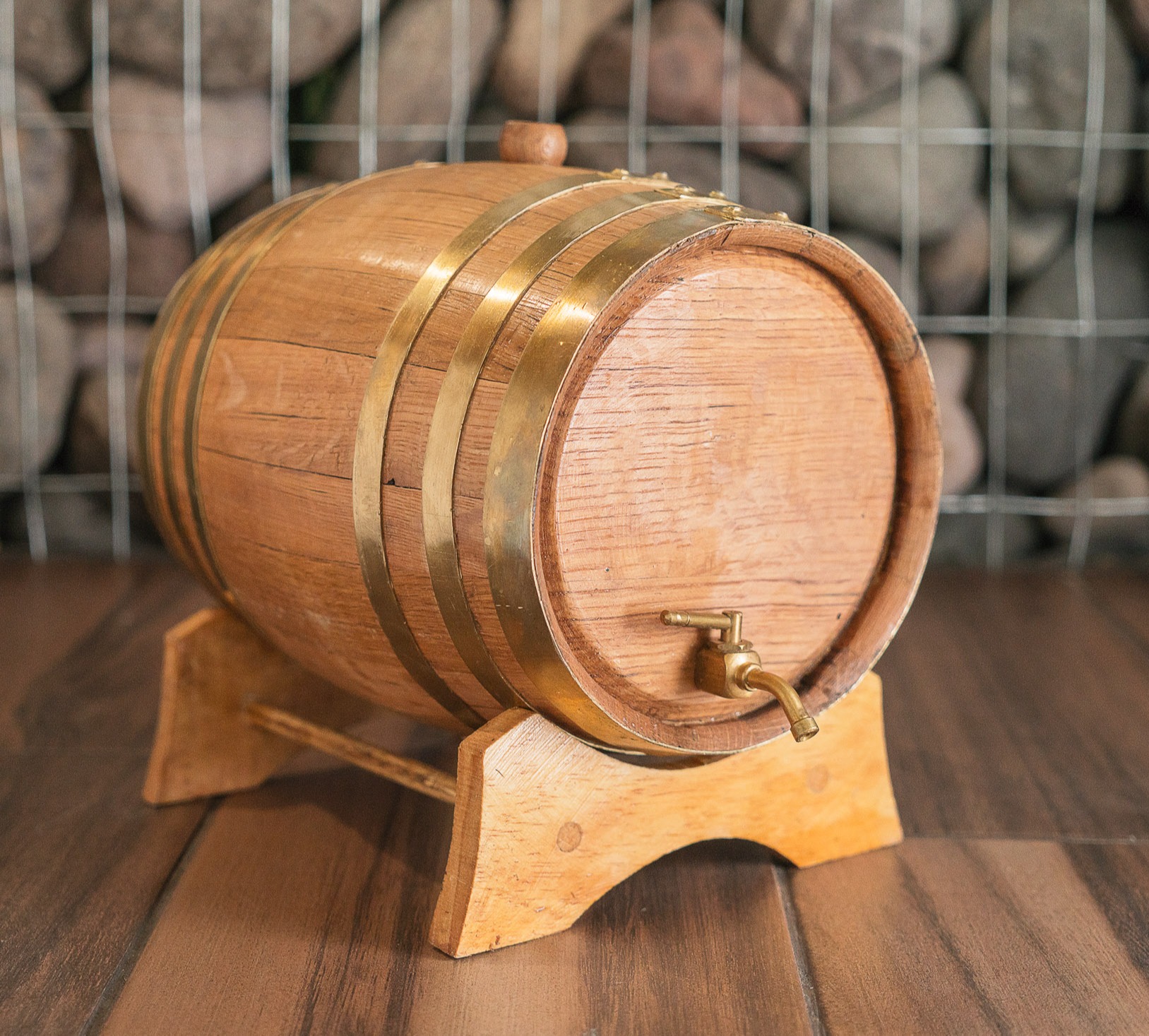 Golden wooden barrel displayed on wooden floor against stone wall