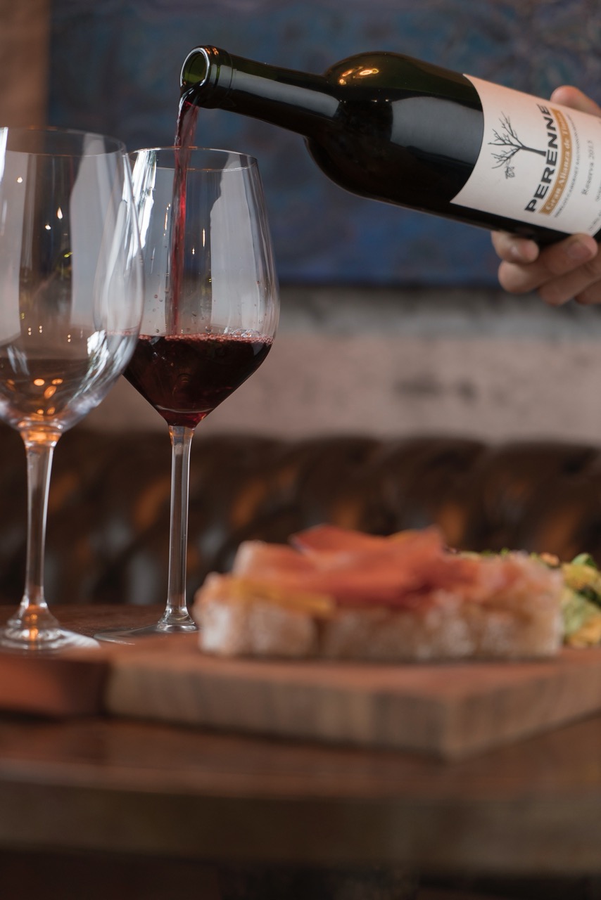 Red wine being poured into a glass accompanied by a tapas board