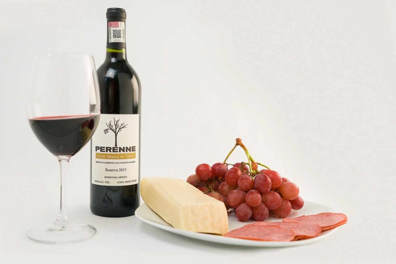 Red wine bottle with glass and charcuterie board featuring grapes, cheese, and salami on white background