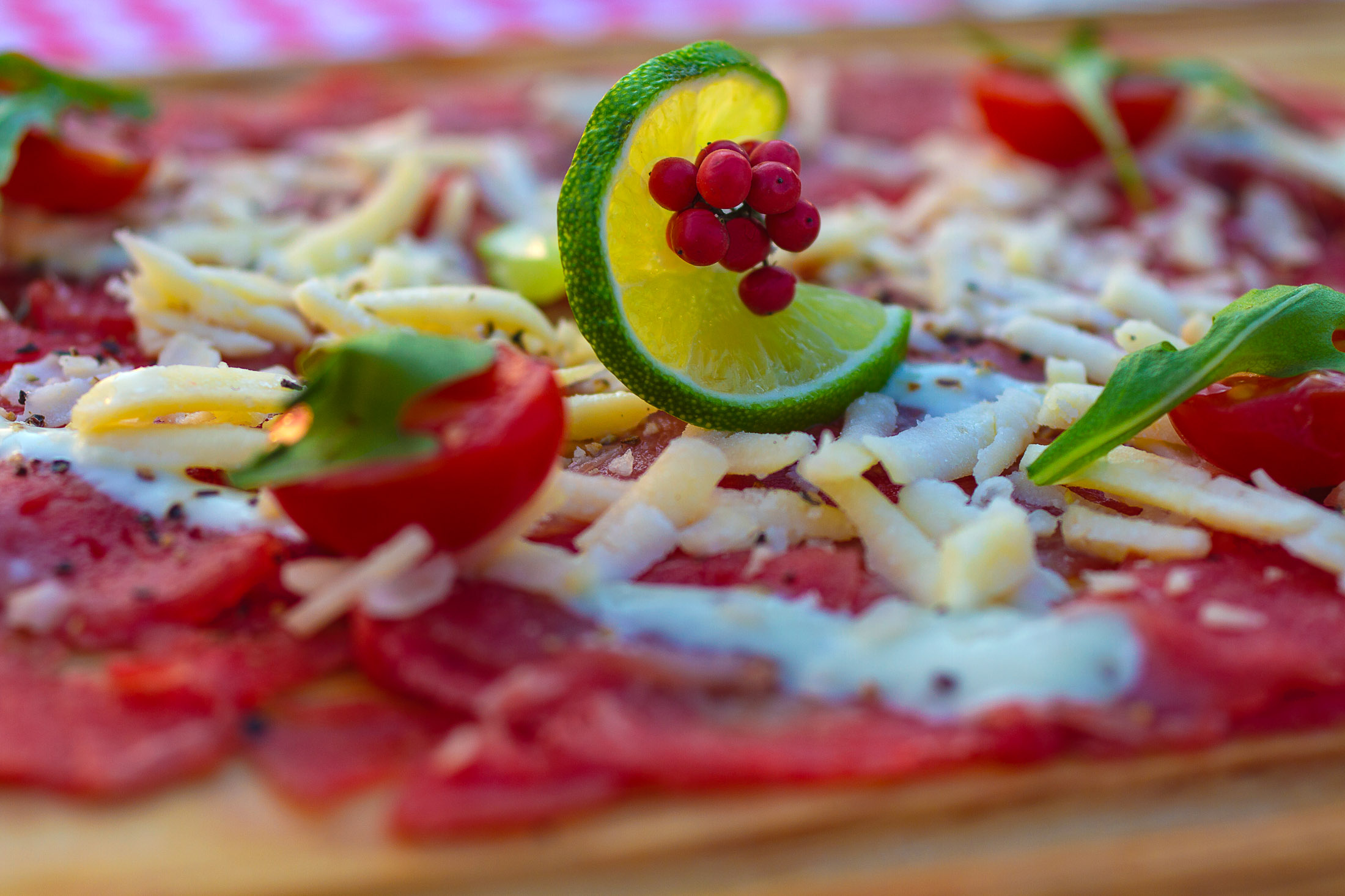 lose-up of beef carpaccio on wooden board with lemon slice and red pepper in countryside environment