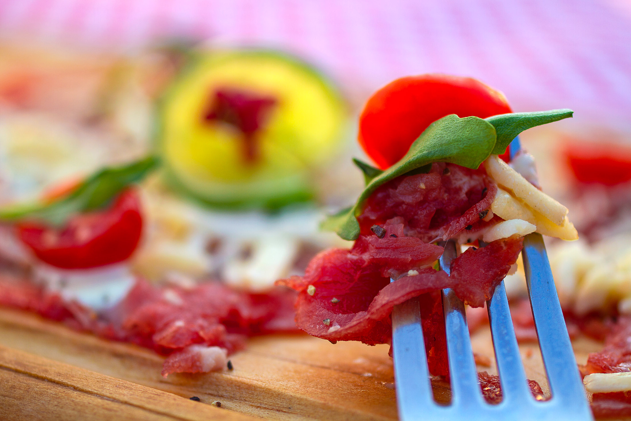 Beef carpaccio on fork ready to eat with basil leaf and cherry tomato in rustic outdoor setting